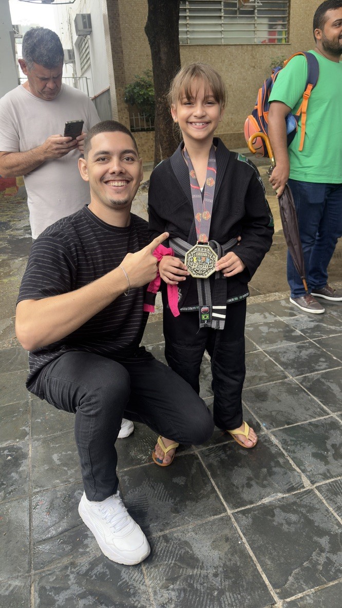 Thiago Antunes ao lado de uma criança de kimono preto com uma medalha de jiu-jitsu