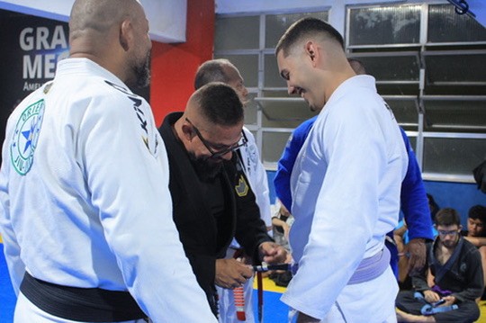 Thiago Antunes ao lado de um professor de roupa preta durante sua graduação de faixa roxa