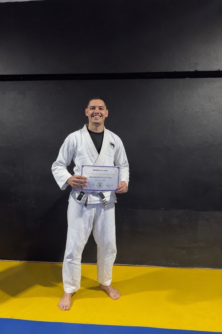 Thiago Antunes de kimono e faixa roxa segurando seu certificado
